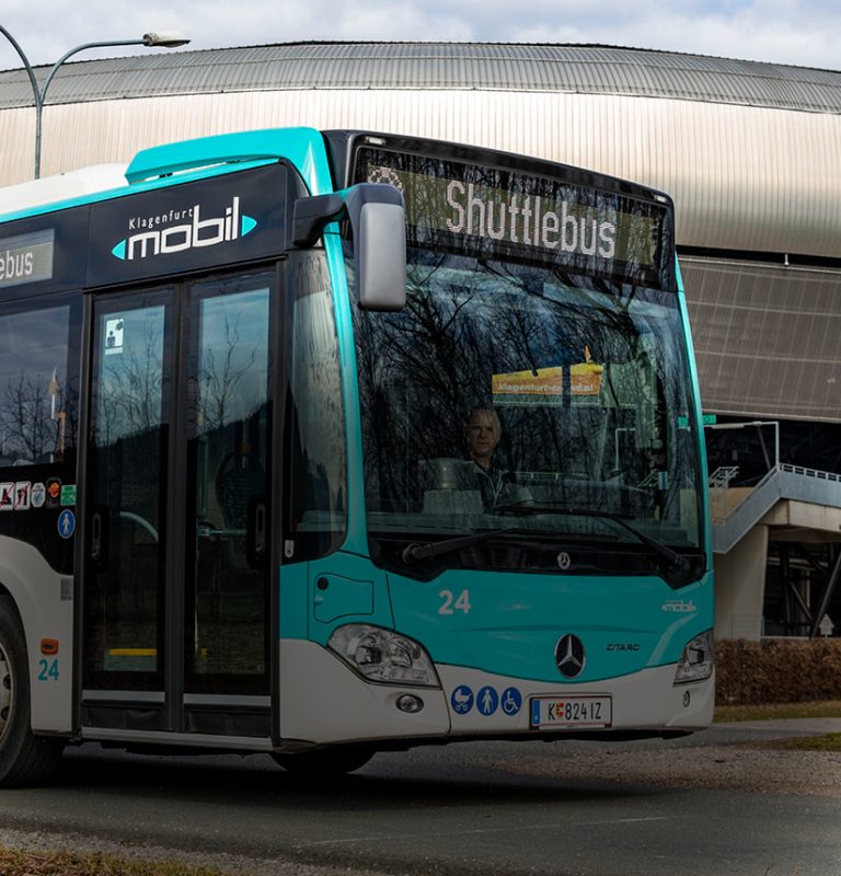 Im Hintergrund sieht man die Süd-/Ostseite des Klagenfurter Stadions. Davor steht ein von links kommender KMG-Bus mit dem Zielschild 