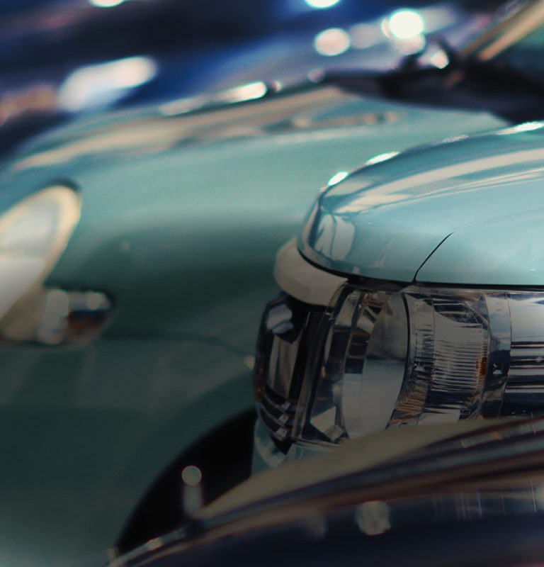 Man sieht drei parkende Autos von der Seite. die Fronten von zwei türkisen und dahinter eines dunklen Autos